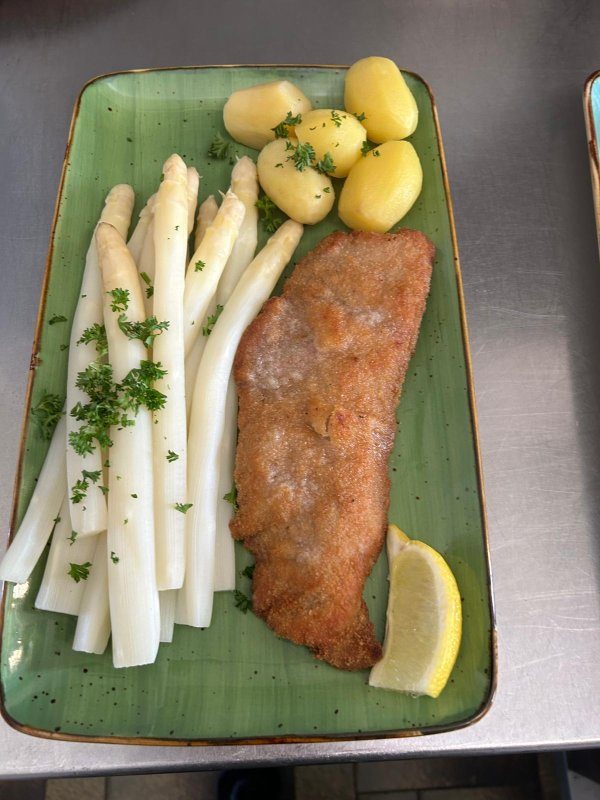 Paniertes Schnitzel mit frischem Spargel, Salzkartoffeln und Zitrone auf grünem Teller